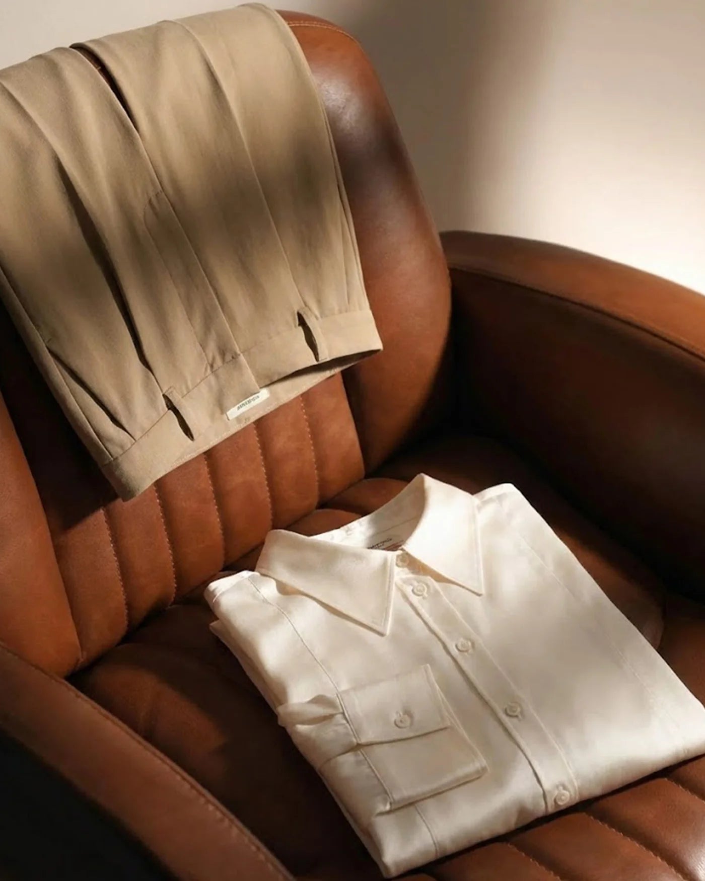 Folded beige pants and white shirt on a brown leather chair. scotch & Soda UK
