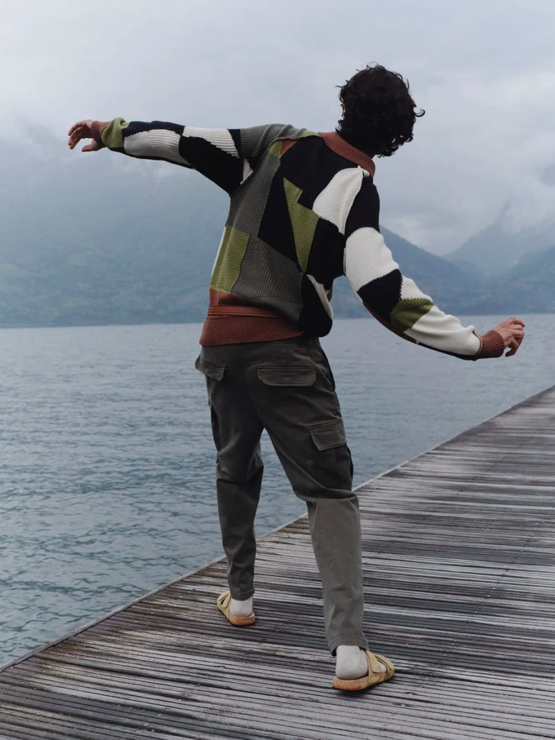 Person standing on a wooden dock by a lake, wearing a patterned sweater and pants.