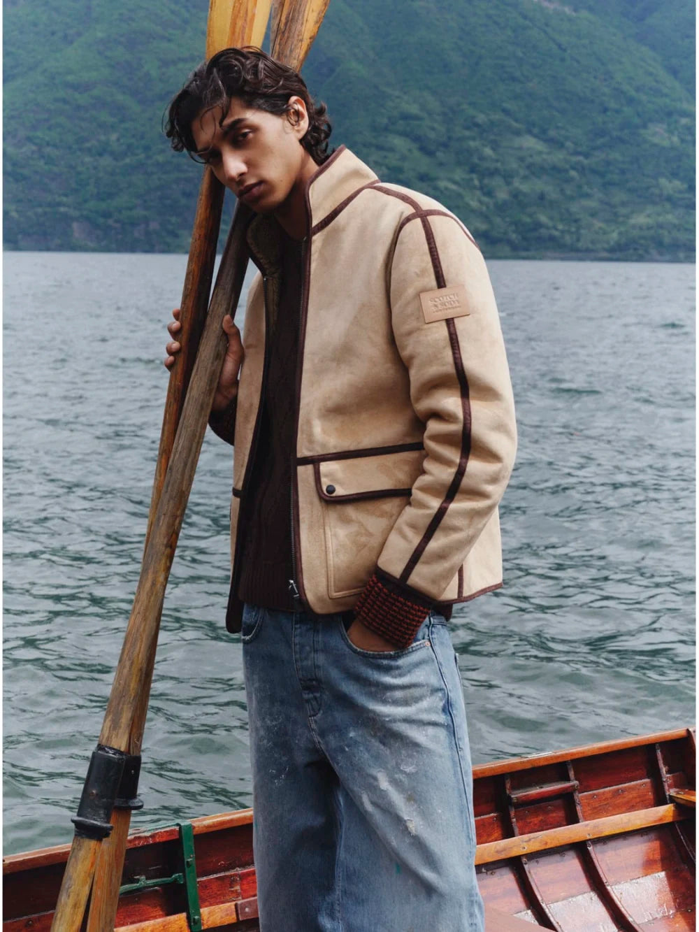 Person in a beige jacket holding a paddle on a boat with a scenic background