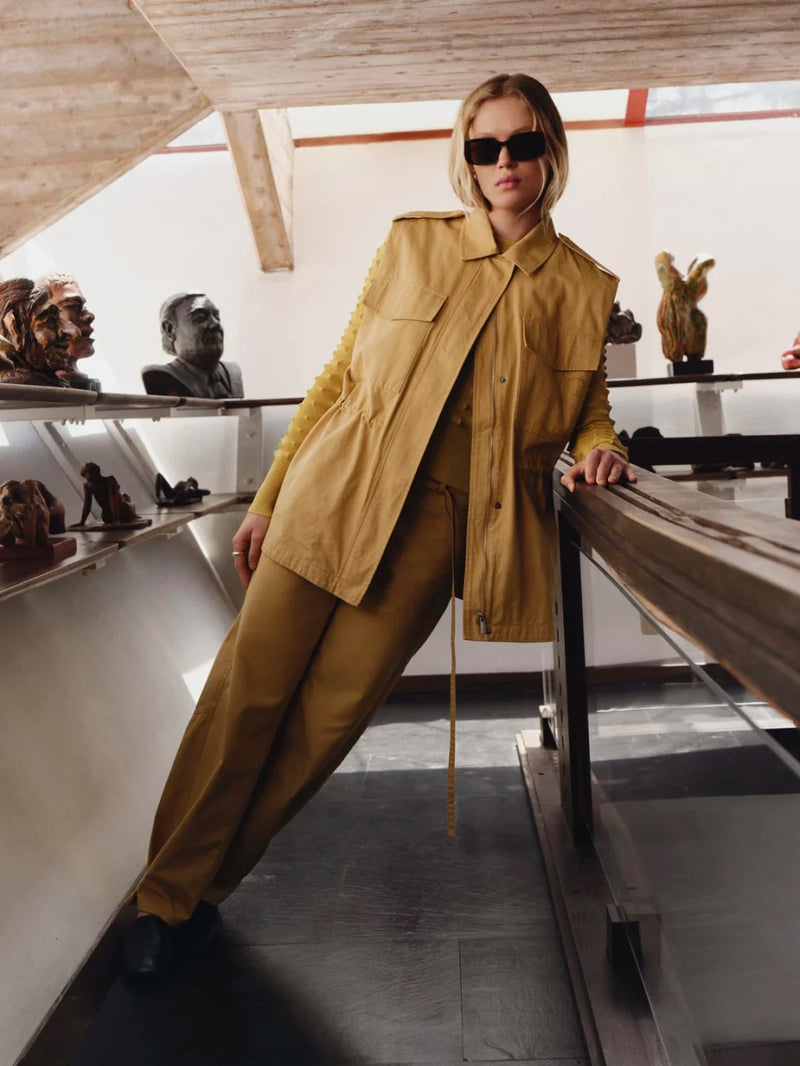 Person wearing a yellow trench coat and sunglasses in an indoor setting with sculptures.